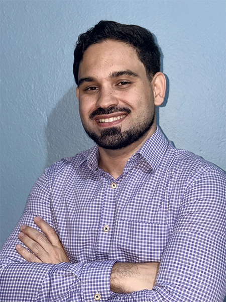 foto do raphael salgado sorrindo, em pé, com uma parede azul atrás